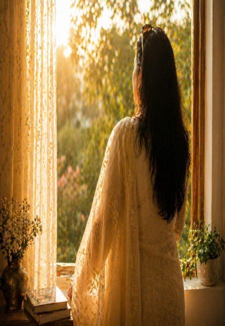 Woman standing by a sunlit window, symbolising reflection, presence, and inner peace